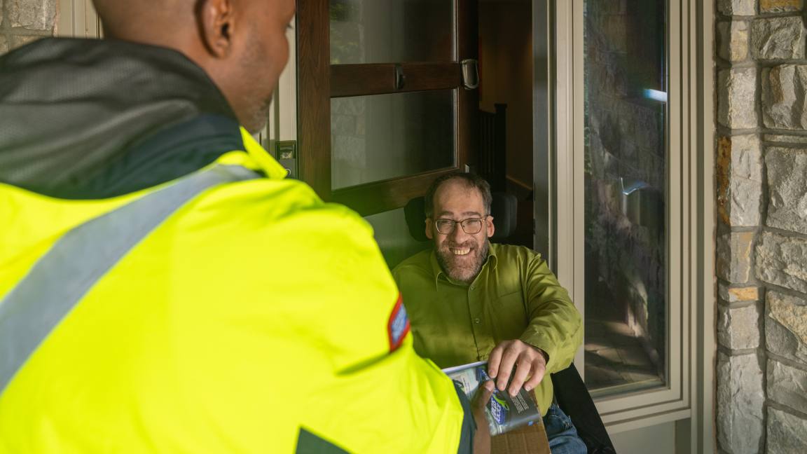 Un homme en fauteuil roulant accepte une livraison d’un facteur à sa porte d’entrée