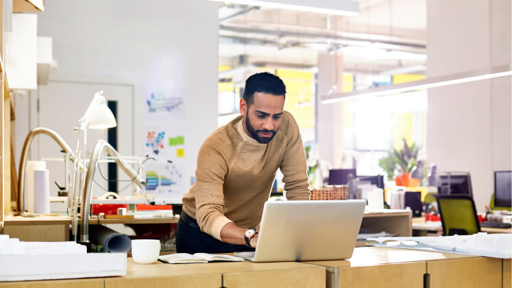 Un homme est debout et travaille sur un ordinateur portable dans un espace de bureau ouvert.